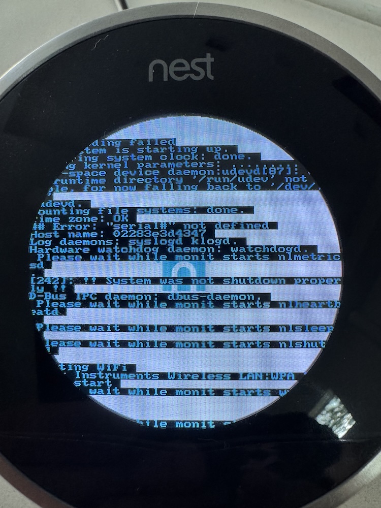 Photo of a Nest Thermostat with kernel panic messages displayed over the Nest boot logo.