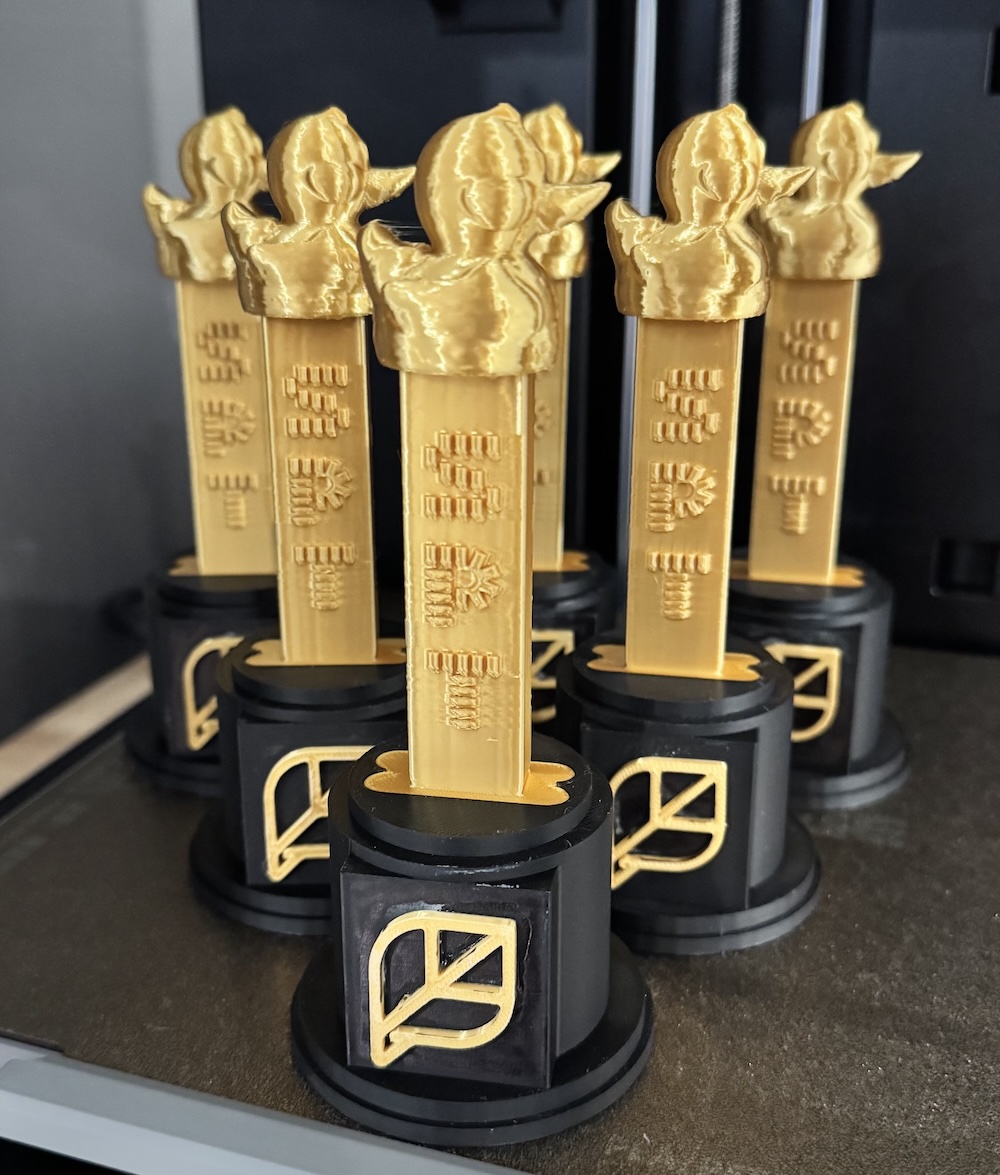Six 3d-printed gold trophies with a gold duck Pez dispenser.
